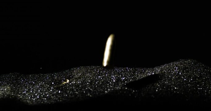 Falling golden 9mm bullets on silver black sand with black background, close up slowmotion 