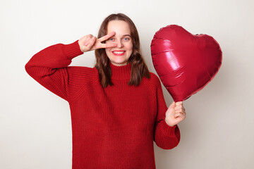 Cheerful smiling brown haired adult woman wearing red sweater holding heart shape balloon posing...