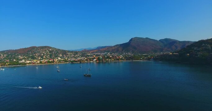 Flying over a bay filled with sailing yachts and boats anchored in the calm water off the coast of Zihuatanejo, Mexico