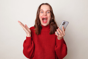 Online social network. Overjoyed Caucasian woman wearing warm red sweater using mobile phone...