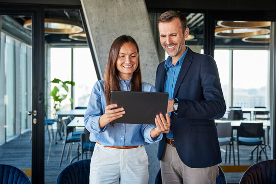 Happy businesswoman and businessman discussing over tablet PC