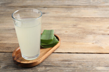 Tasty aloe juice in glass and cut fresh leaves on wooden table, closeup. Space for text