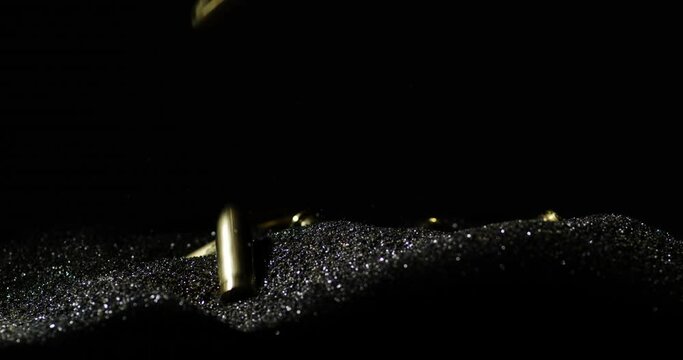 Slow motion shot of falling 9mm parabellum bullets on black sand in studio,close up