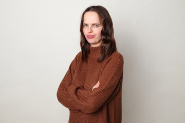 Displeased brown haired adult woman wearing brown sweater posing isolated over gray background...