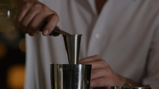 Closeup shot of a bartender measuring liquor into a jigger and pouring it into a metal shaker