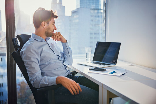 Thoughtful young businessman sitting with laptop at desk