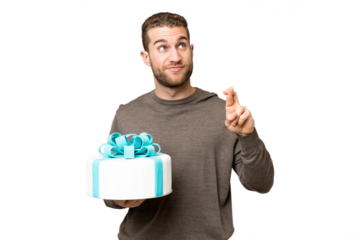 Young handsome blonde man holding birthday cake over isolated chroma key background with fingers crossing and wishing the best