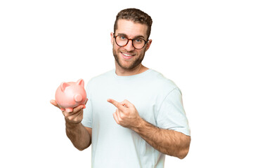Young man holding a piggybank over isolated chroma key background and pointing it