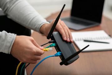 Man inserting cable into Wi-Fi router at wooden table indoors, closeup