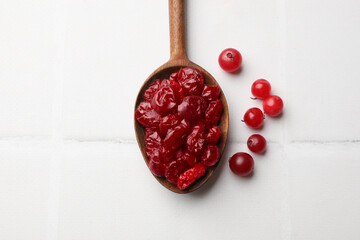 Tasty dried cranberries in spoon and fresh ones on white tiled table, top view