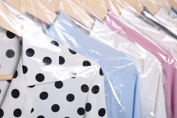 Dry-cleaning service. Many different clothes in plastic bags hanging on rack, closeup