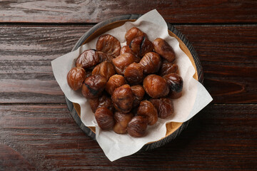Roasted edible sweet chestnuts in bowl on wooden table, top view