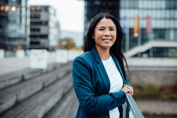 Happy businesswoman standing near railing at office park
