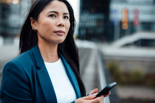 Thoughtful businesswoman holding smart phone