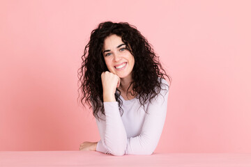 Smiling young woman sitting at table against pink background