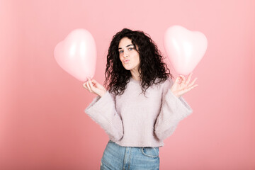 Woman puckering and holding heart shaped balloons against pink background