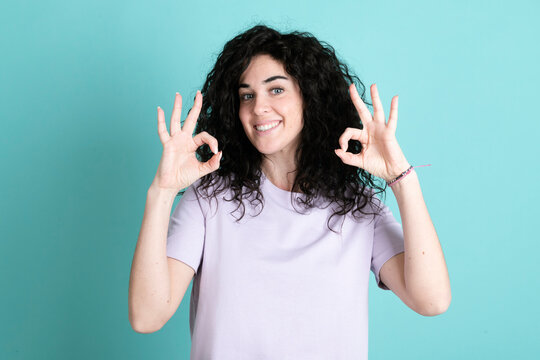 Smiling young woman gesturing OK sign against turquoise background