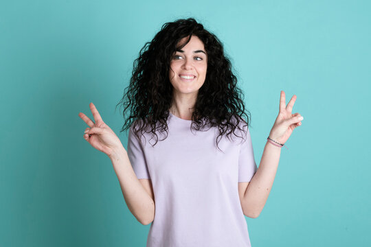 Smiling young woman gesturing peace sign against turquoise background