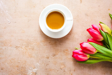 Eine Tasse Kaffee und pinke Tulpen auf einem braunen Tisch. Draufsicht.