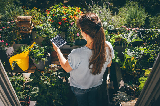 Woman holding solar battery near plants in balcony