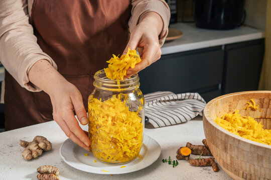 Woman putting sauerkraut in glass jar at kitchen counter