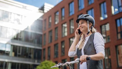 Beautiful middle-aged woman commuting through the city by bike, phone calling on smartphone. Female...
