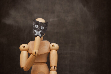 Wooden mannequin holding mask with mouth closed, concept of free speech problems.