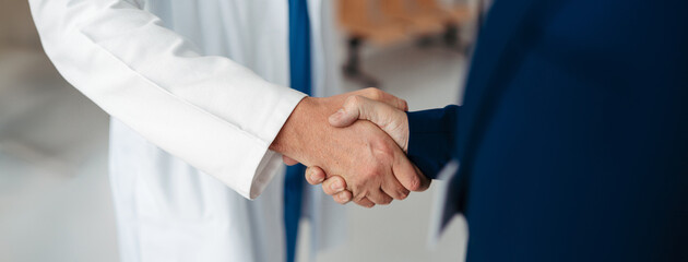 Close up of pharmaceutical sales representative shaking hands with doctor in medical building....