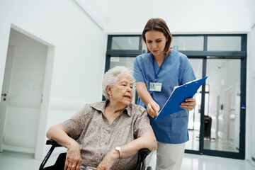 Nurse talking with senior woman, admitting a patient to the hospital, filling documents....