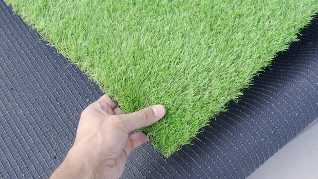 Close up of hand holding an artificial grass roll. Greenering with an artificial turf
