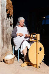 Full body of concentrated aged woman making thread with old wooden thread maker spinning
