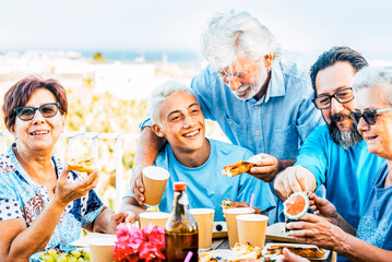Multigenerational family having lunch on a terrace on a beautiful sunny day. 18 year old boy laughs with his grandparents celebrating. Lifestyle and family concept.​