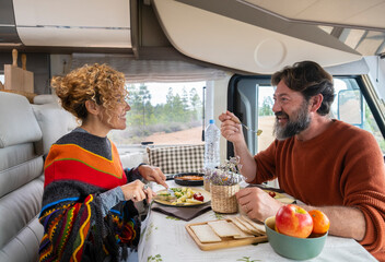Couple of travelers sitting at the table in a camper having lunch and relaxing . Bearded man and...