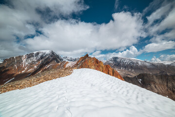 Snowfield on stony mountain ridge and vivid sharp pinnacle in sunlight. Shiny pointy peak of gold...