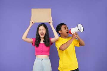 Young amazed couple two friends family Asian man and woman together hold in hand megaphone scream...