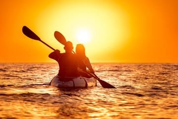 Young couple is walking on kayak or canoe at sunset sea beach - obrazy, fototapety, plakaty