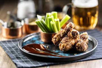 Fried chicken legs with celery sticks and draft beer on plate in pub or restaurant