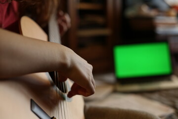 Close up, cinematic, young musician learns to play classical guitar at home. Online lesson, green chromakey on a computer screen