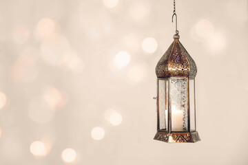 Hanging copper burning Moroccan lantern. Festive pale beige background with glittering bokeh...