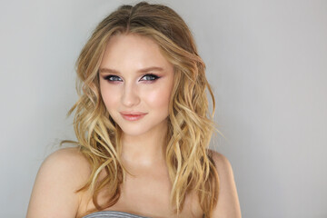 Naklejka premium Young beautiful woman with blonde curly hair on grey background