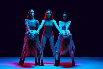 Young woman, professional dancers in bodysuits performing high heel dance against black background in neon light. Concept of modern dance style, creativity and beauty, art, hobby