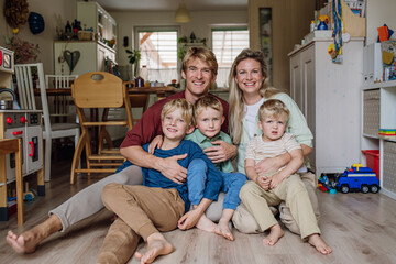 Portrait of family sitting on floor in living room. Beautiful mother with her three sons and...
