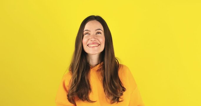 Young pathos woman pointing cheerfully while giving her imaginary money, in front of a yellow background. The concept of pouring money without thinking. It makes it rain by throwing money into the air