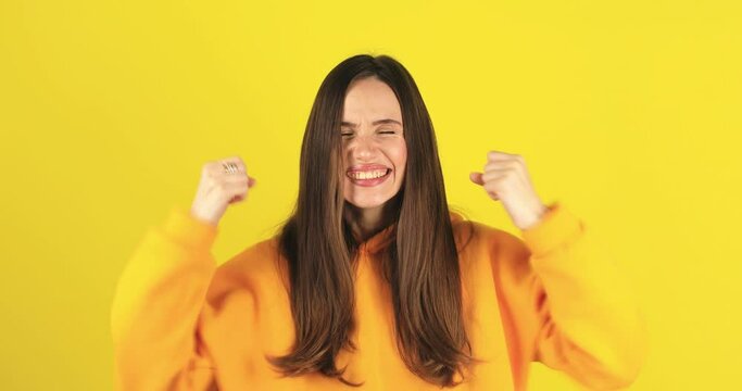 Amazed excited woman hairstyle in yellow hoody open mouth in surprise looking at camera with big eyes, shocked isolated on yellow background. Oh my god wow, yes gesture, win symbol.