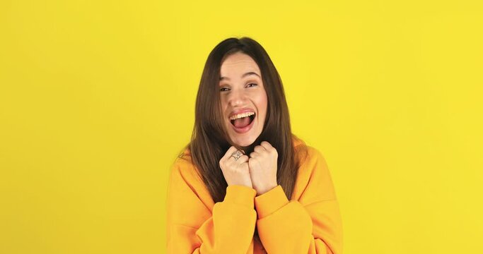 Amazed excited woman hairstyle in yellow hoody open mouth, screaming in surprise looking at camera with big eyes, shocked isolated on yellow background. Oh my god wow, yes gesture, win symbol.