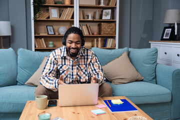 Young African American man with headset having web call using laptop computer and smartphone...