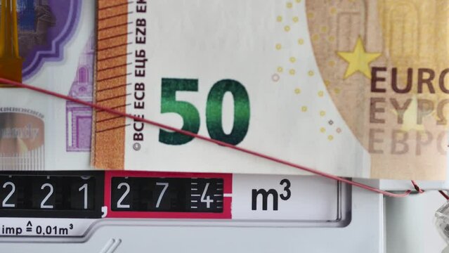 rotating numbers in a working home gas meter with 50 euro banknote on top, macro