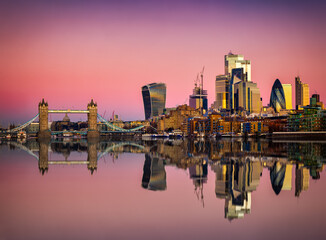 The skyline of the City of London and Tower Bridge during pink dawn and sunrise with relfections in...