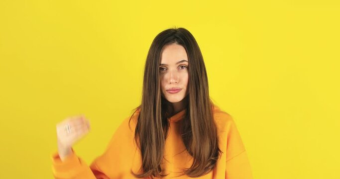 Brunette indignant woman showing blah blah blah gesture with hands isolated on studio yellow background. Empty promises, blah concept. Lier, not interested. Annoyed girl making bla bla hand gesture.