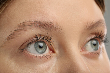 Woman with long eyelashes after mascara applying against grey background, closeup